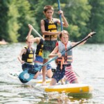 boys paddle boarding on lake at summer camp
